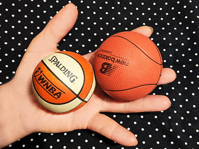 A hand holding two mini basketballs--WNBA Spalding and New Balance, both are from the early 2000s. Diameters of the balls are a little over 2 inches.